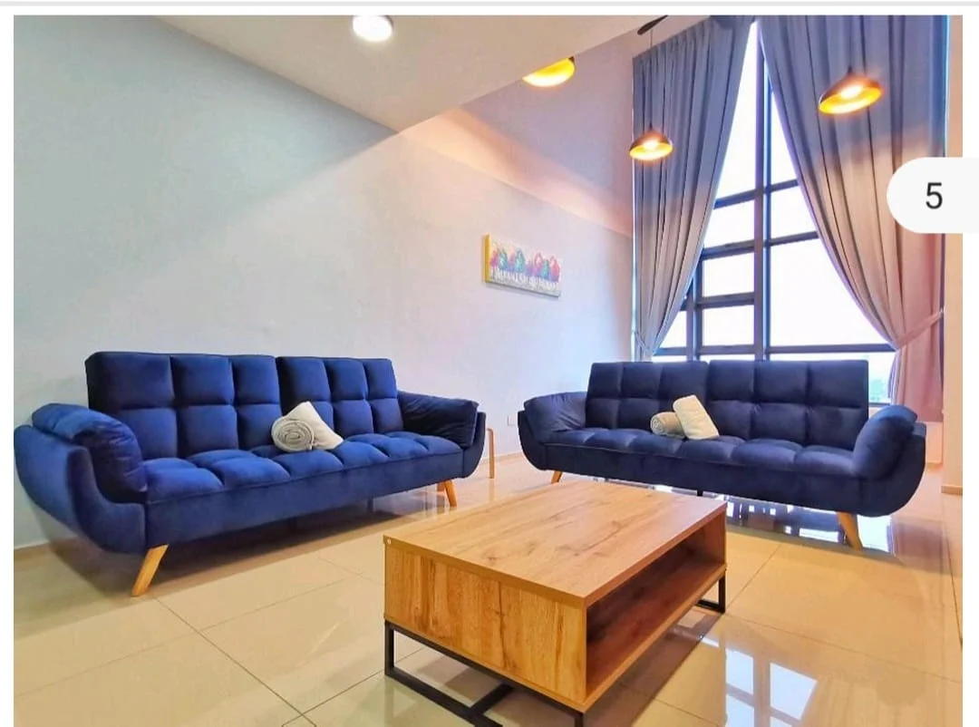 Living features: two blue fabric sofas with tufted design, wooden coffee table with black metal frame, large floor-to-ceiling windows, light grey painted walls, cream tiled flooring, two pendant lights hanging from ceiling, sheer curtains in light blue, decorative artwork on wall; style: modern.
